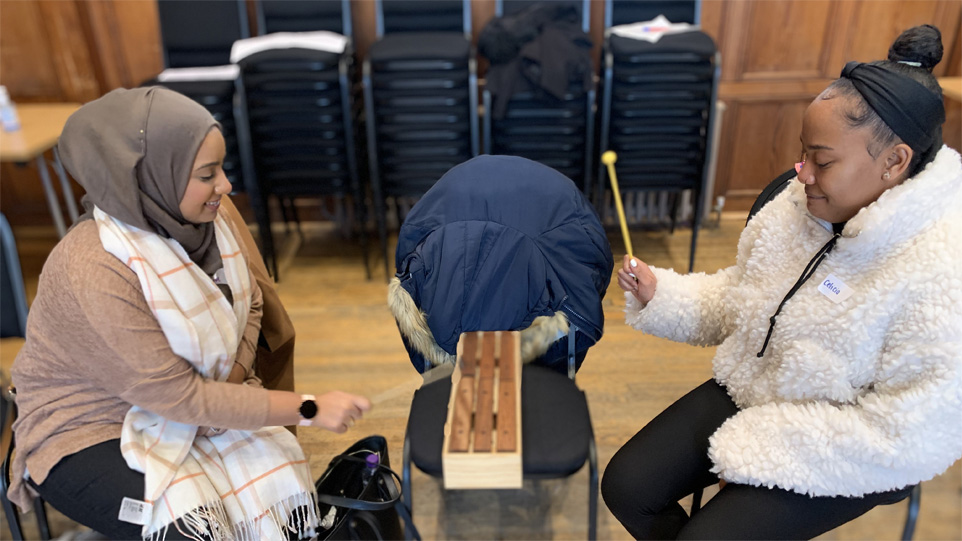 Two women sitting on chairs playing on a xylophone.